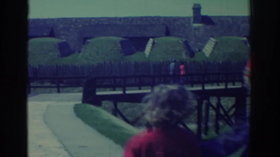 Final 1971 frame shows two visitors near a wooden bridge, with grassy fort ramparts, cannons, and a path behind them.