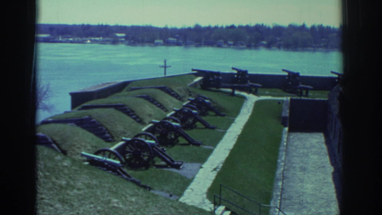1971 8mm view near Niagara Falls showing a fort courtyard with cannons on grass, stone walls, and a broad river in the background.