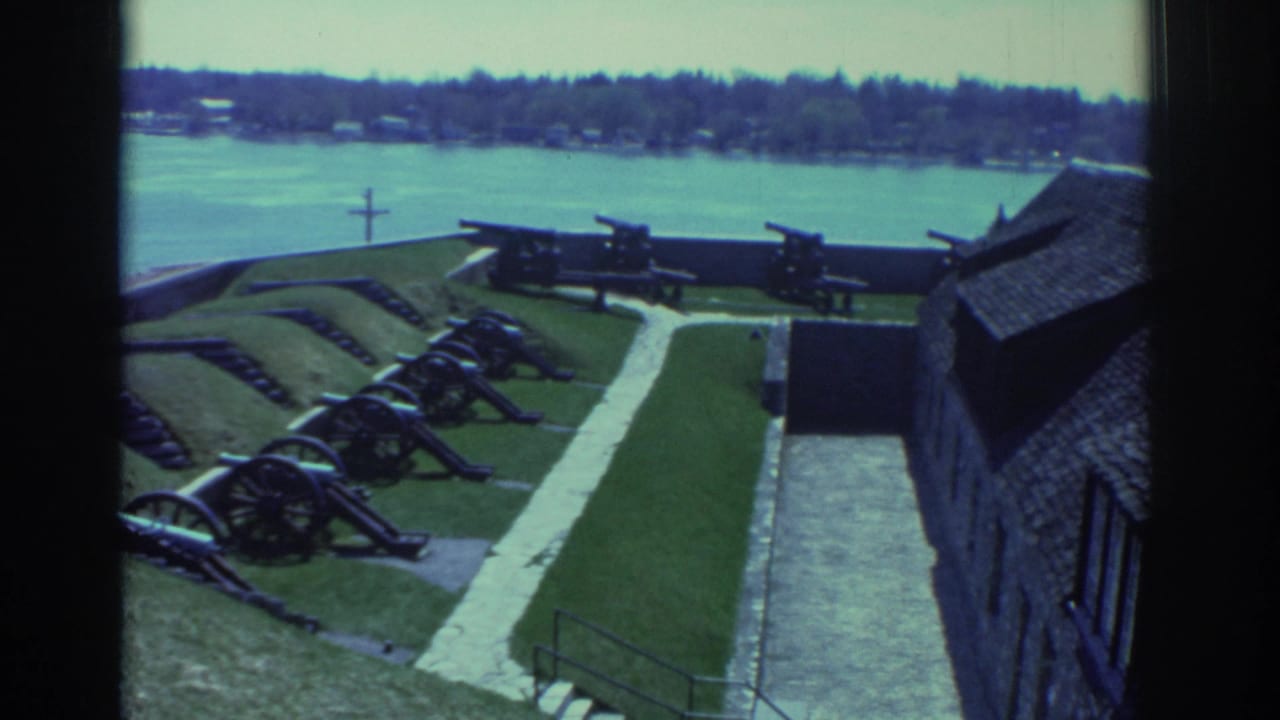 Cannons and fort walls seen through a dark window frame with river and shoreline behind.