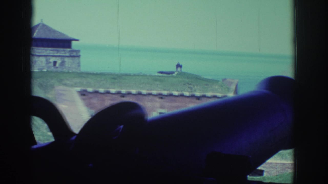 1971 8mm view near Niagara Falls, with cannon silhouettes inside a fort opening and a stone building beside the water.