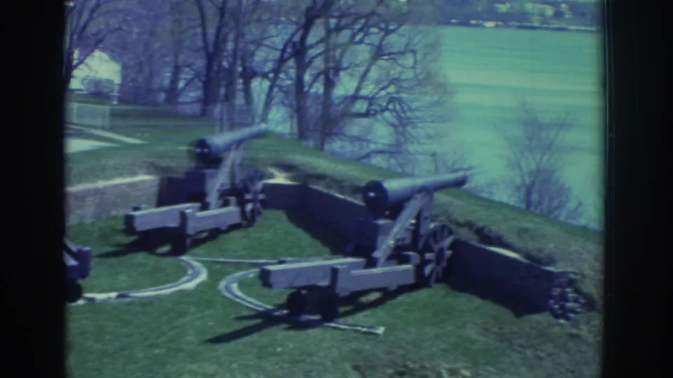 1971 8mm view of cannons displayed on a grassy historic fort rampart near Niagara Falls, with water and trees beyond.