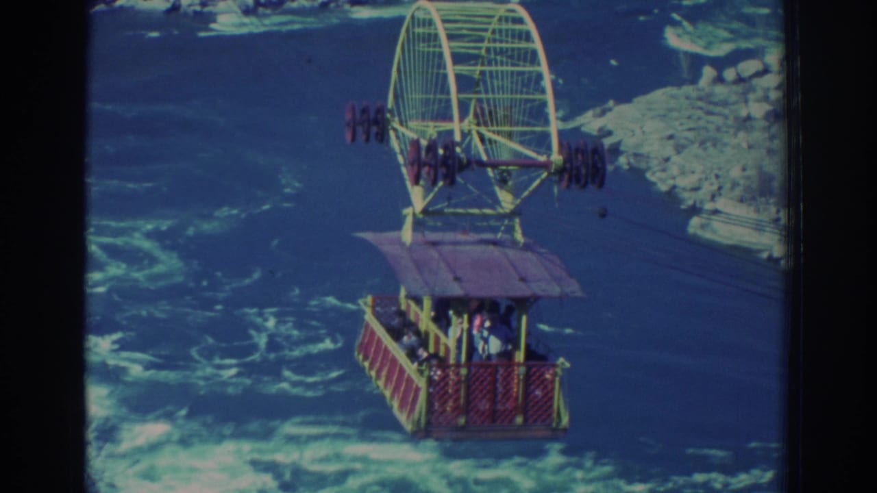 1971 Niagara Falls home-movie frame showing a red cable car with passengers suspended over turbulent blue-green water.