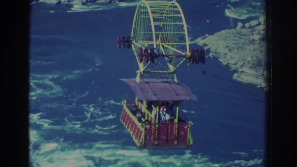 1971 Niagara Falls home-movie frame showing a red cable car with passengers suspended over turbulent blue-green water.