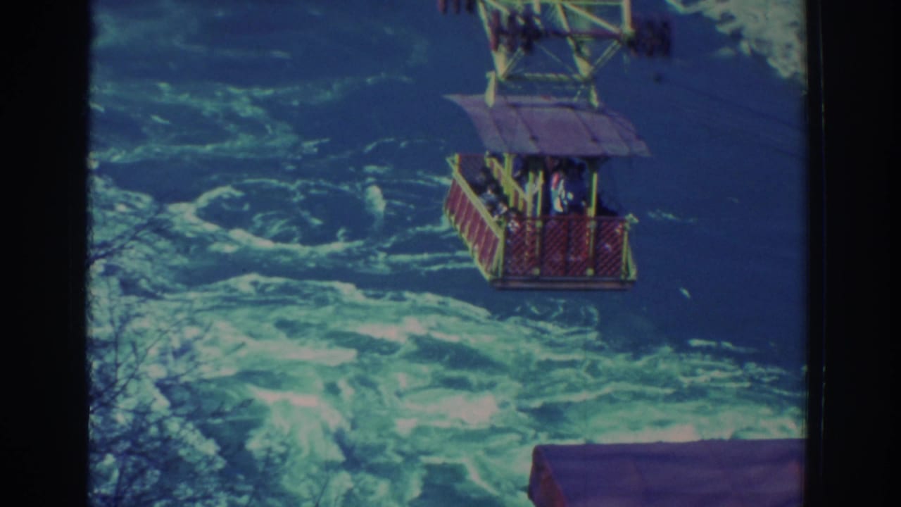 1971 Niagara Falls frame with the suspended sightseeing car partly high in view over foaming rapids.