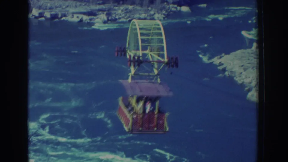 1971 Niagara Falls frame showing the suspended red cable car and large yellow wheel assembly over the river current.