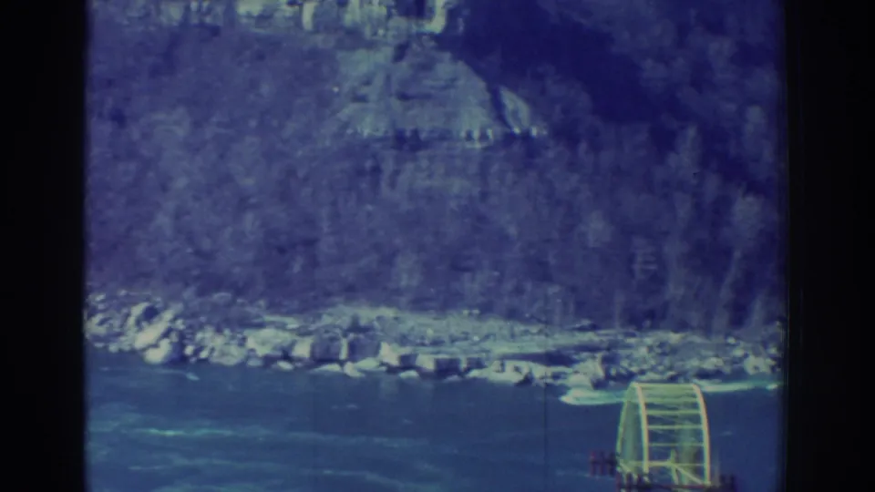 A distant 8mm frame places the sightseeing gondola low in view against the Niagara Gorge river and tree-covered slopes.