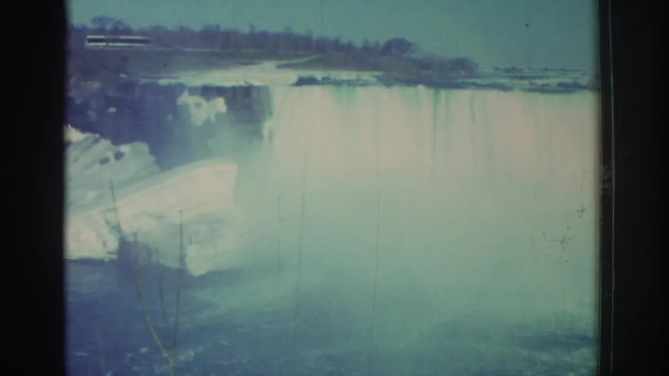 Wide 1971 Niagara Falls view showing the waterfall, heavy mist, river edge, and distant tree line.