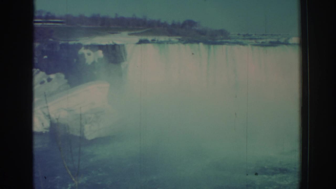 1971 8mm home-movie frame of Niagara Falls from New York, showing the waterfall curtain, rising mist, distant tree line, and contact-sheet borders.