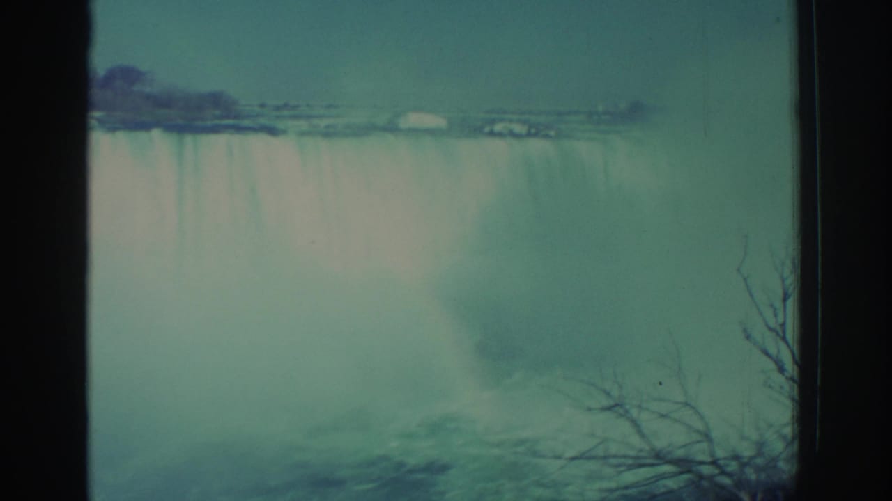 Waterfall and mist seen through dark film-frame edges with bare branches at the lower right.