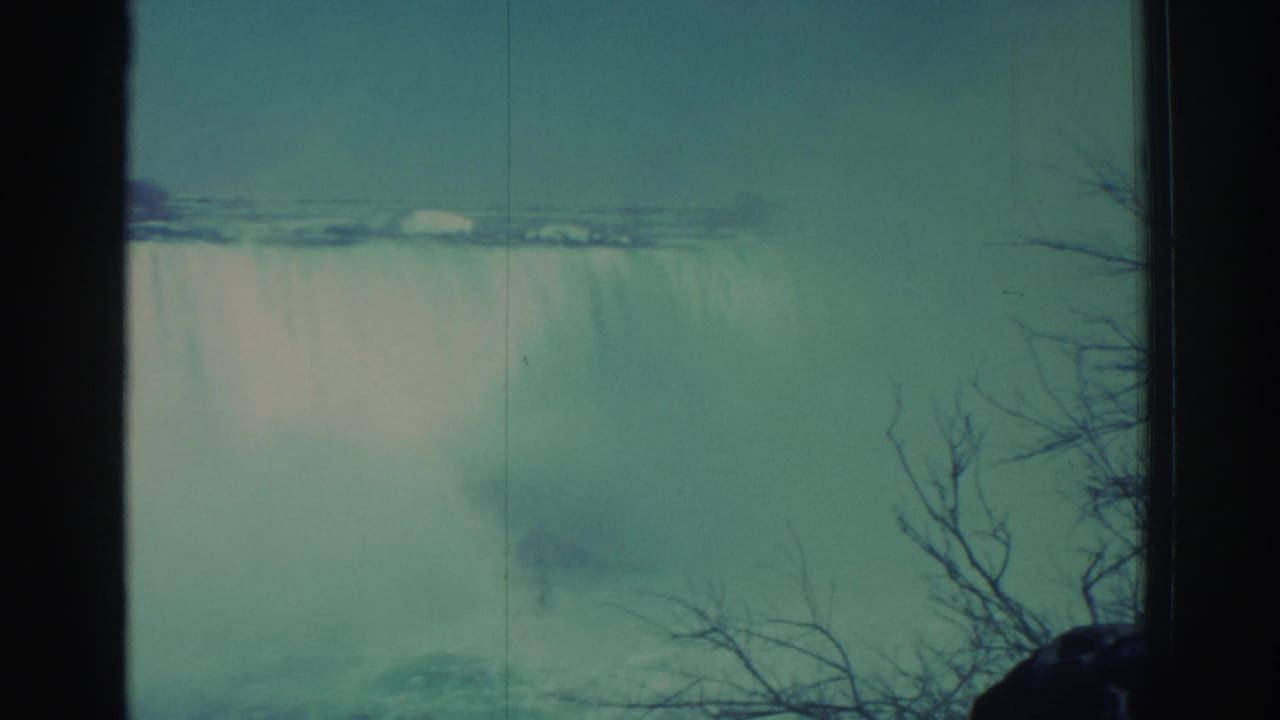Waterfall and mist with bare branches along the right side and dark vertical film border.