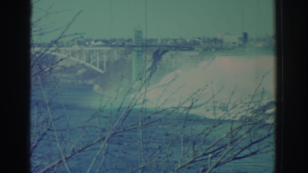 Falls and mist seen below a bridge, with bare branches crossing the foreground.