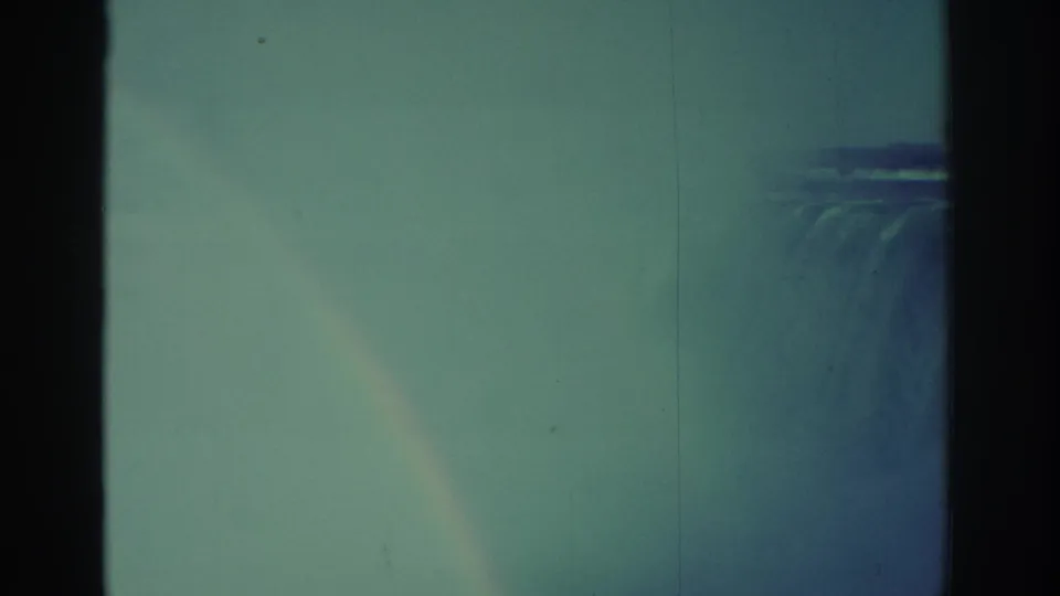 1971 Niagara Falls frame with a faint rainbow visible in the mist beside the waterfall, softened by faded 8mm color.