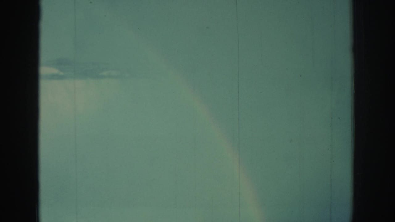 Rainbow and mist over Niagara Falls, framed by dark vertical film borders and faded color.