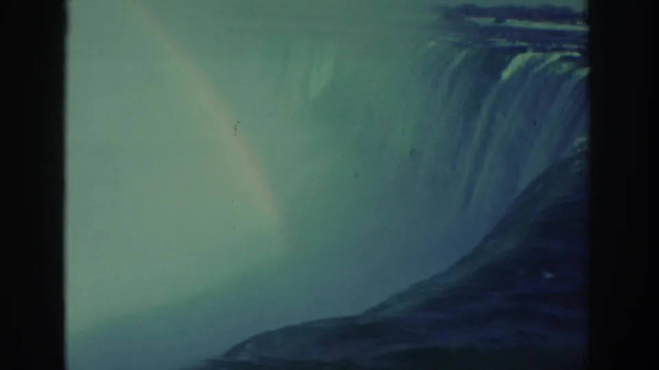 1971 8mm frame of Niagara Falls with the cascade at right, heavy mist below, and a faint rainbow through the spray.