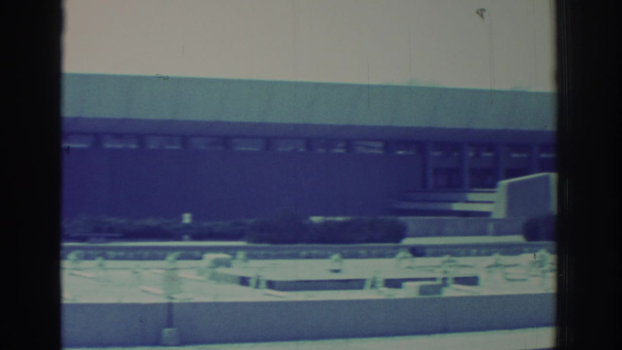 1971 8mm view of a long, low building in Niagara Falls, New York, framed by dark vertical borders and a blue-green film cast.