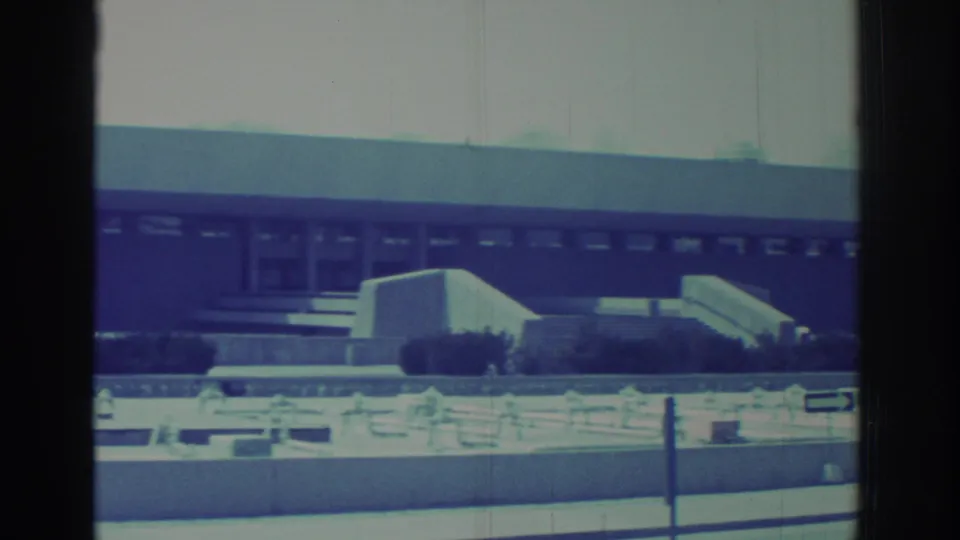 Wide 1971 home-movie frame showing the Hockey Hall of Fame exterior with steps, windows, shrubs, and a pale roadside foreground.