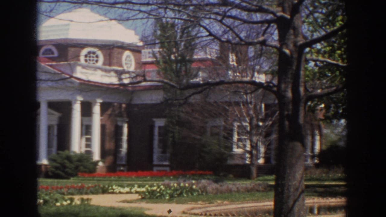 Domed brick mansion and columned entrance viewed past trees and landscaped beds.