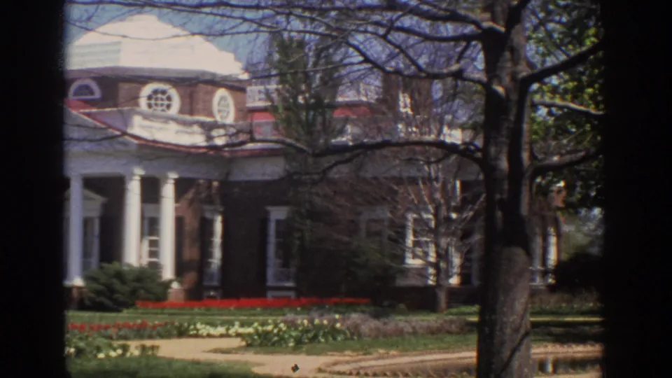 Visitor-shot 1971 view of the domed brick mansion, white portico, bare branches, lawn, and flowerbeds in bright spring light.