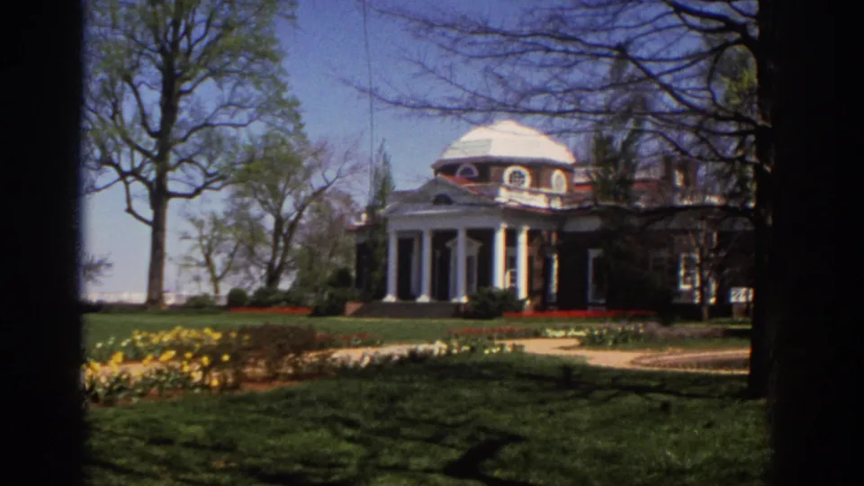 Wide 1971 home-movie view of the Virginia mansion set behind lawn, paths, bare trees, yellow flowers, and a columned portico.