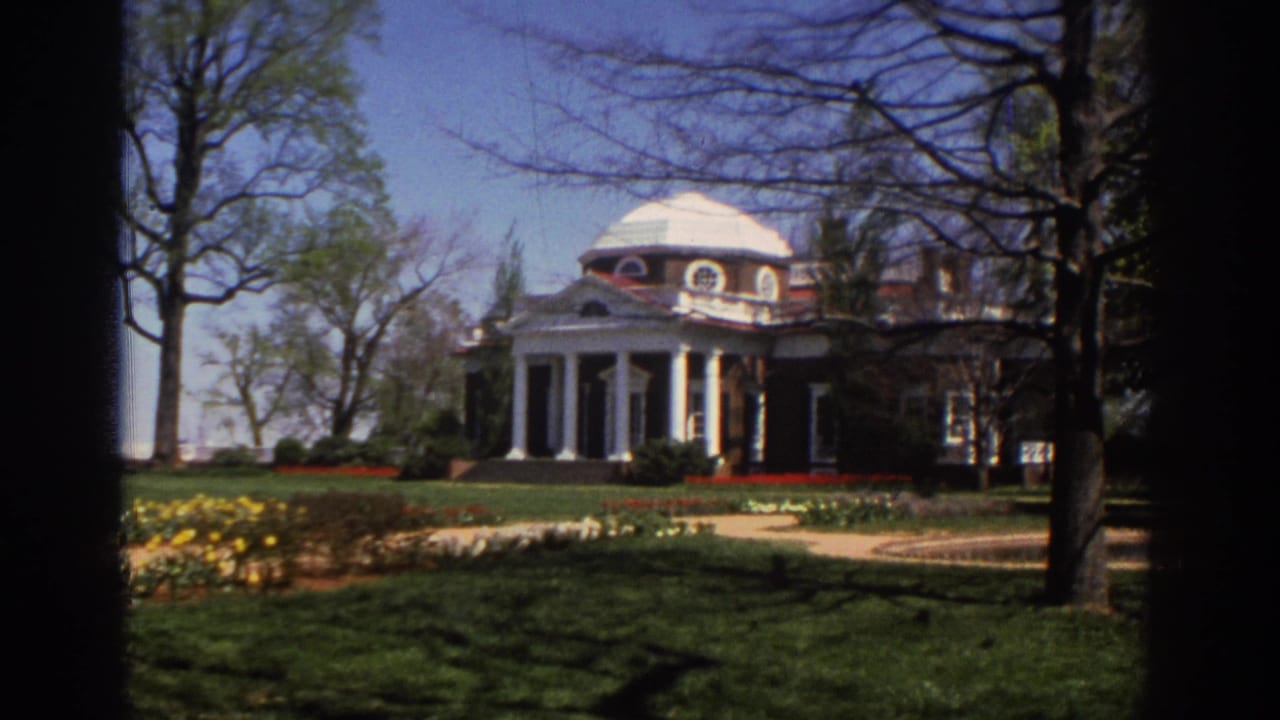 Classical domed building with white columns seen across a lawn and flower beds.