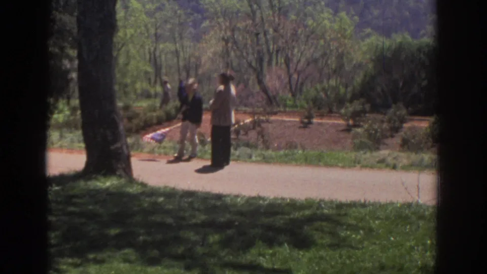 Visitors in 1971 Richmond stand along a paved path beside trees, lawns, and landscaped garden beds.