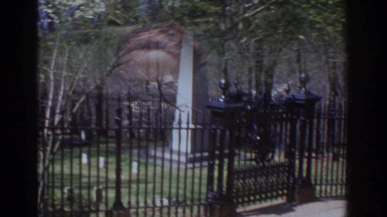 A pale stone obelisk stands behind an ornate black iron gate and fence in a Richmond park or historic grounds setting.