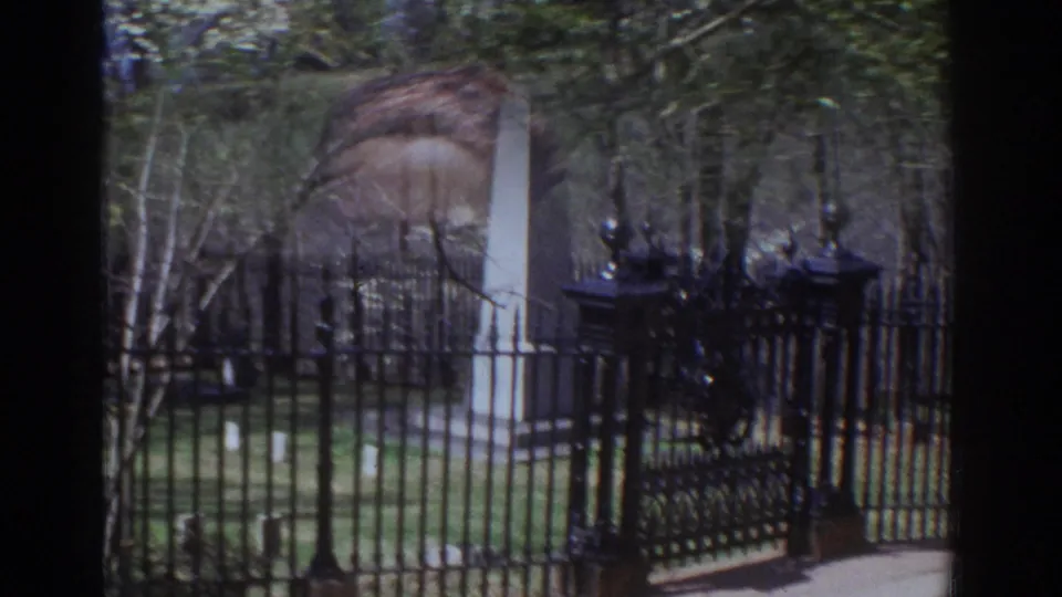 A pale stone obelisk stands behind an ornate black iron gate and fence in a Richmond park or historic grounds setting.