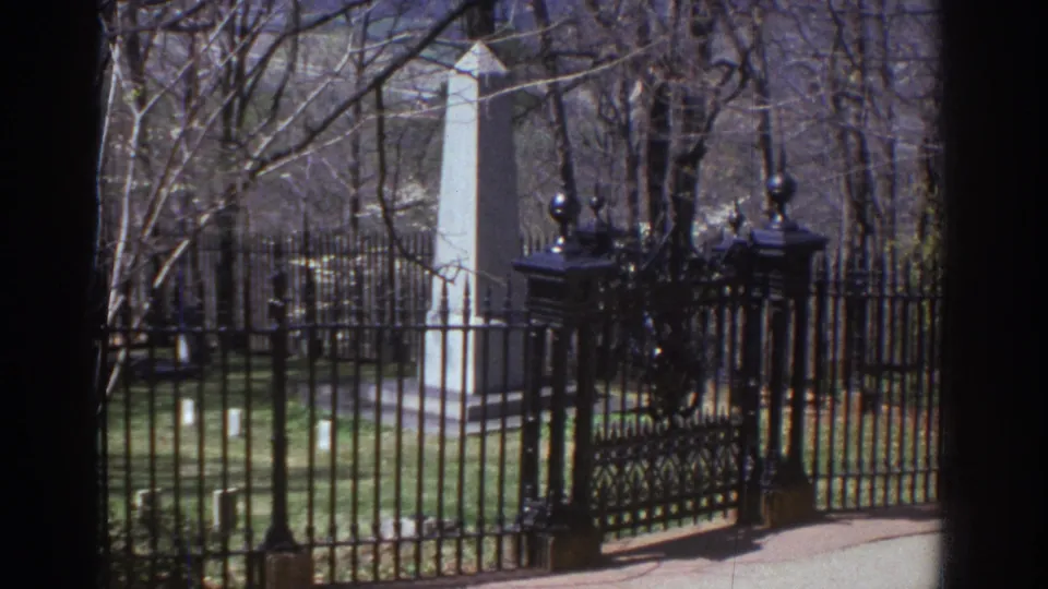 A repeated view of the gated monument shows the black ironwork, pale stone obelisk, bare trees, and grass in the 1971 Richmond footage.