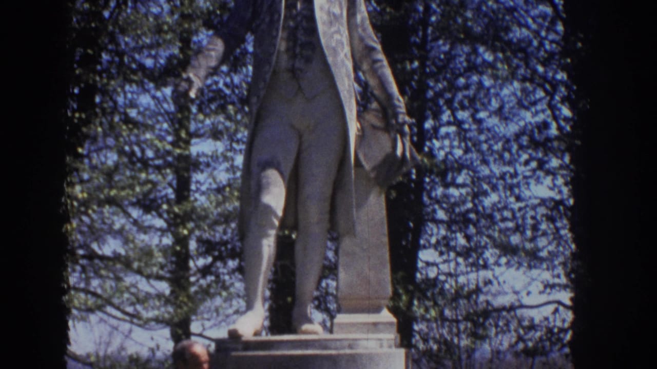 1971 Richmond home-movie frame showing the lower portion of a James Monroe statue framed by trees and blue sky.