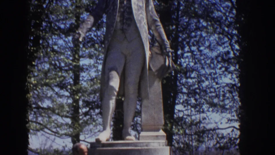 1971 Richmond home-movie frame showing the lower portion of a James Monroe statue framed by trees and blue sky.