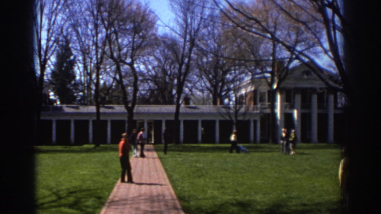 1971 Richmond home-movie frame showing visitors on a brick walkway approaching a grand white-columned estate across a green lawn.