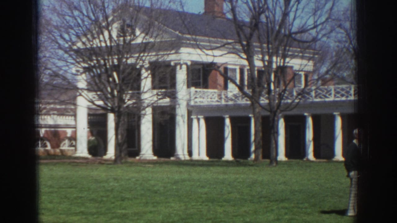 A white-columned mansion stands behind a wide lawn and leafless trees.