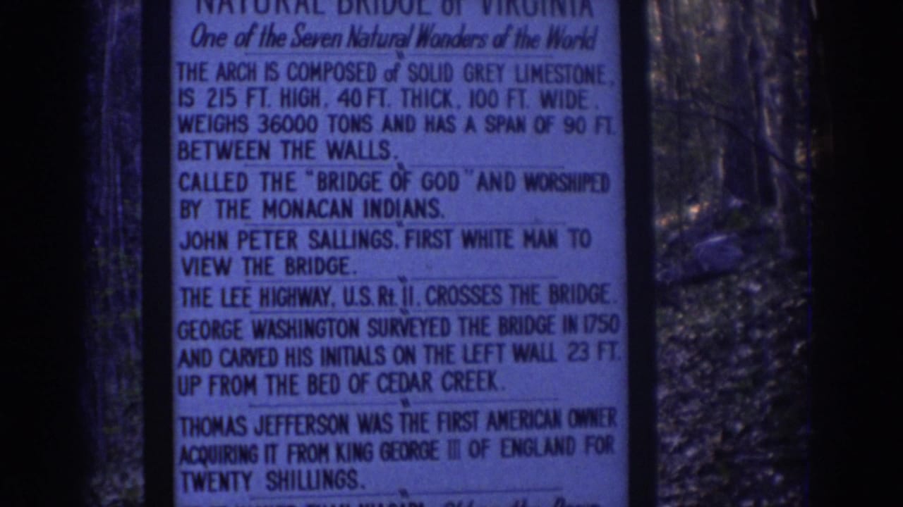1971 8mm frame showing a Natural Bridge information sign at left and the limestone arch visible through trees at right.