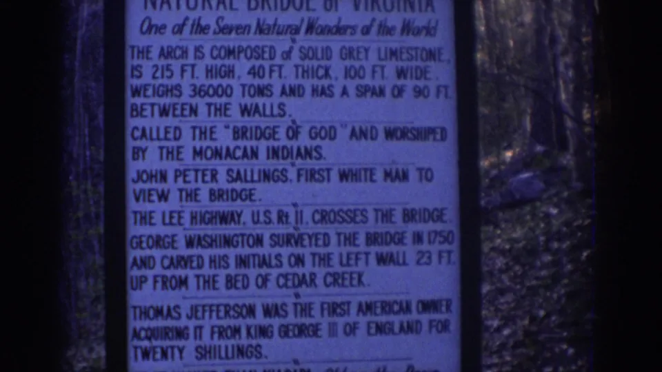 1971 8mm frame showing a Natural Bridge information sign at left and the limestone arch visible through trees at right.