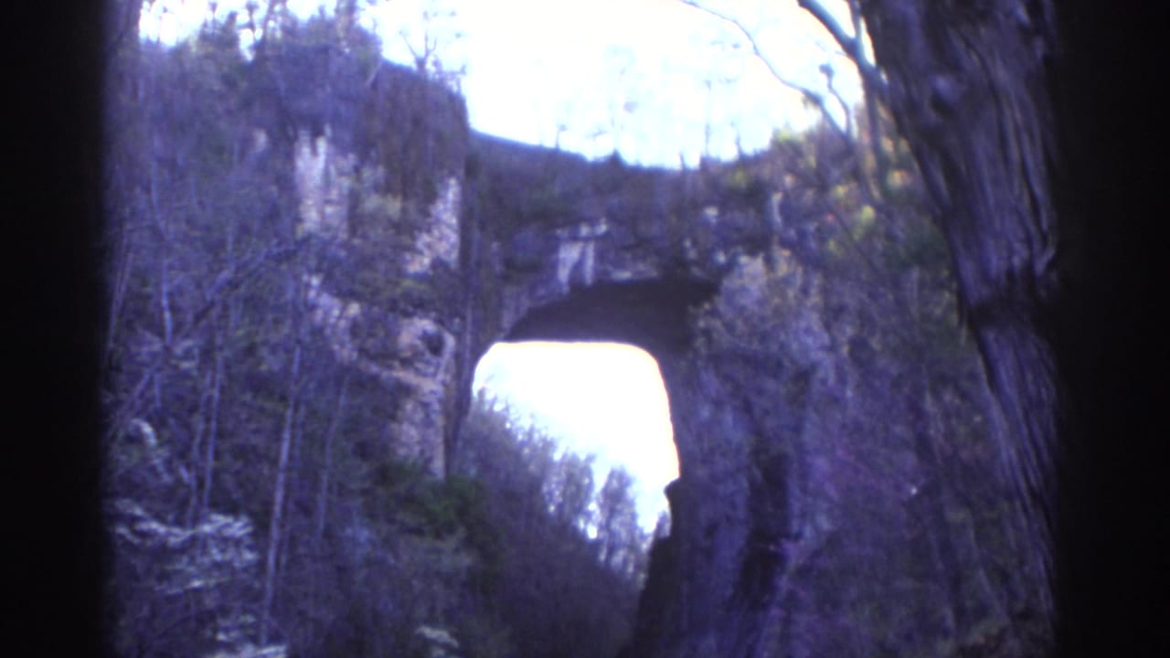 Natural stone arch framed by trees and rock walls.