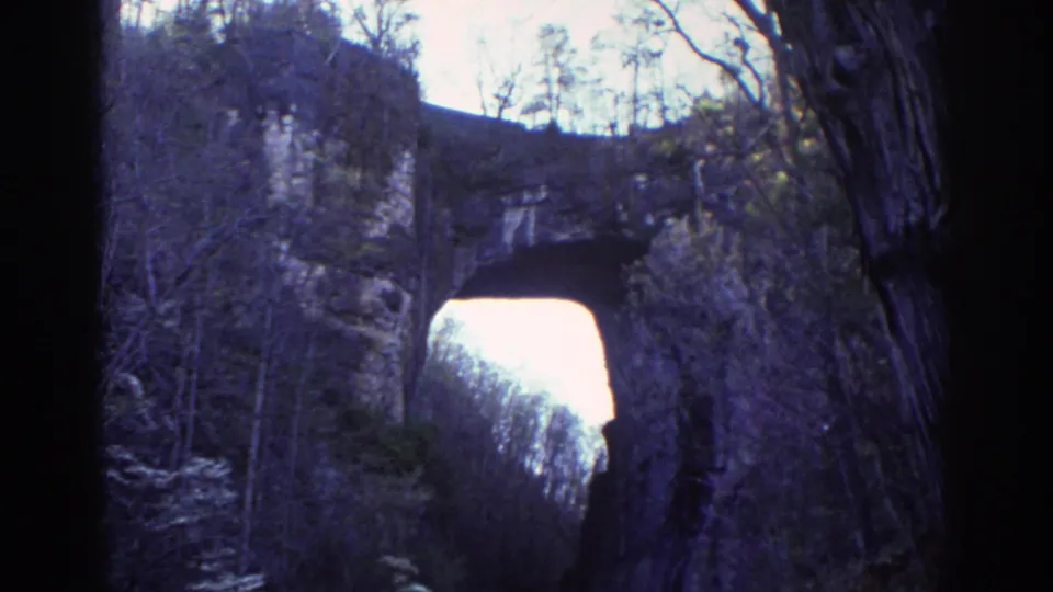 Visitor-shot 8mm frame of Natural Bridge, Virginia, with bare trees and limestone walls surrounding the bright arch opening.