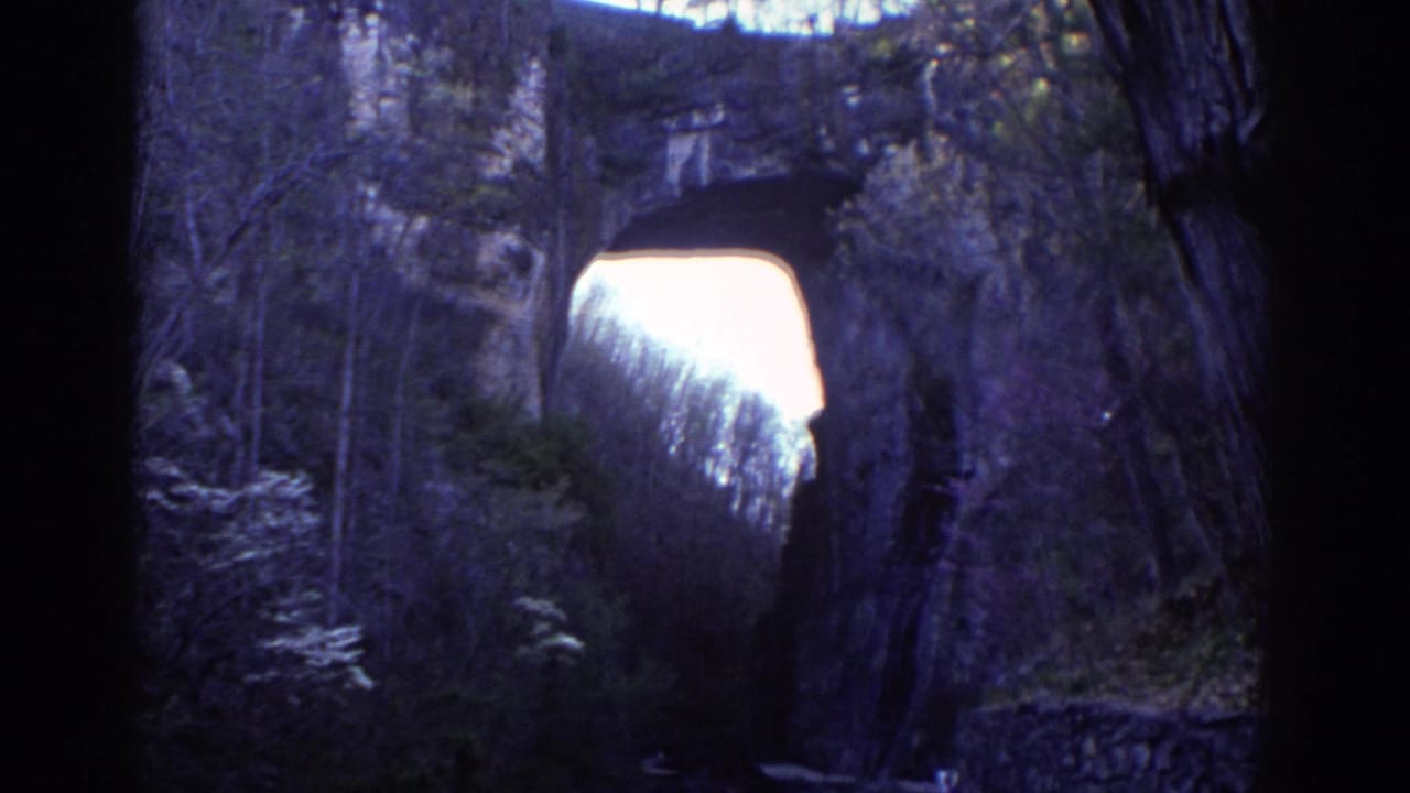 1971 Richmond park footage appears to show a natural stone arch framed by trees and shadowed rock, with bright sky beyond.