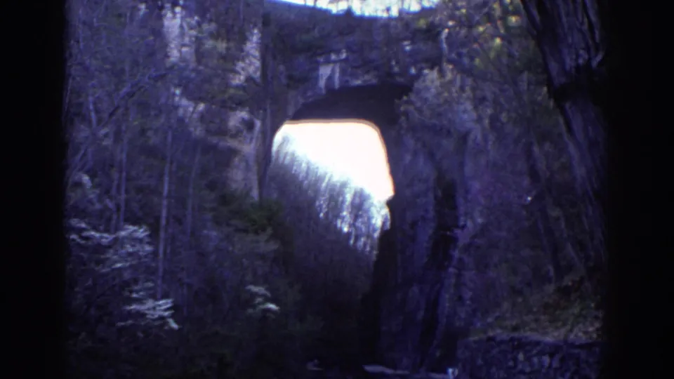 1971 Richmond park footage appears to show a natural stone arch framed by trees and shadowed rock, with bright sky beyond.