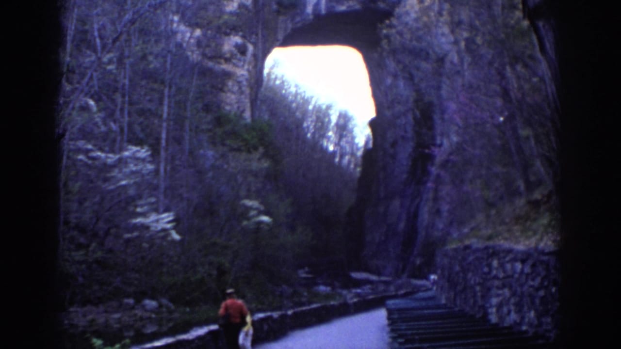 Person in a red top walking on a paved path beside stone walls near a rock arch.