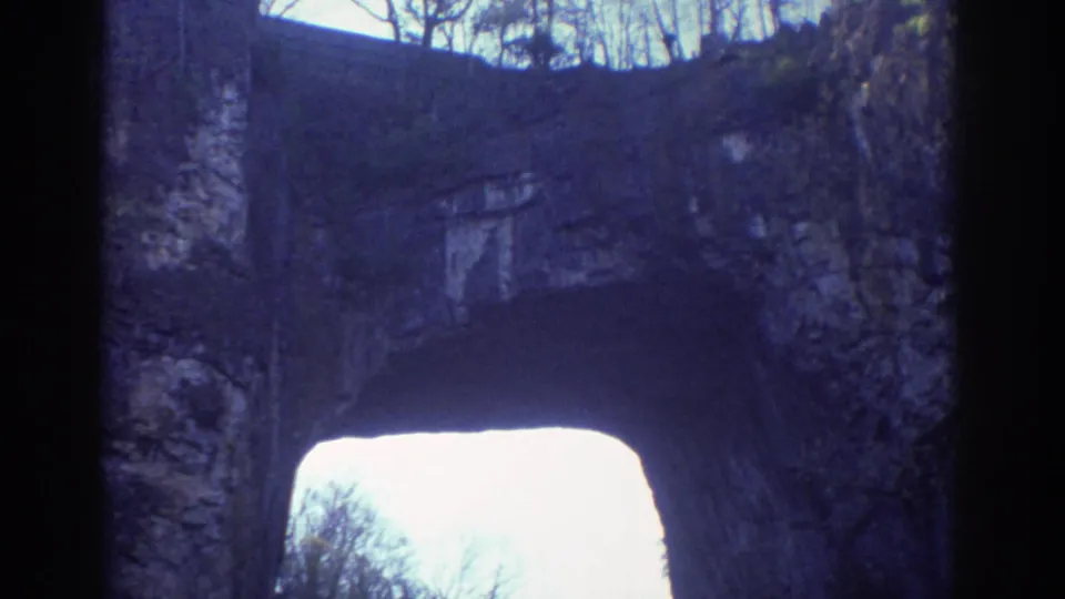 The final frame looks up at the natural stone arch, with dark rock edges, a bright opening, and winter-bare trees beyond.