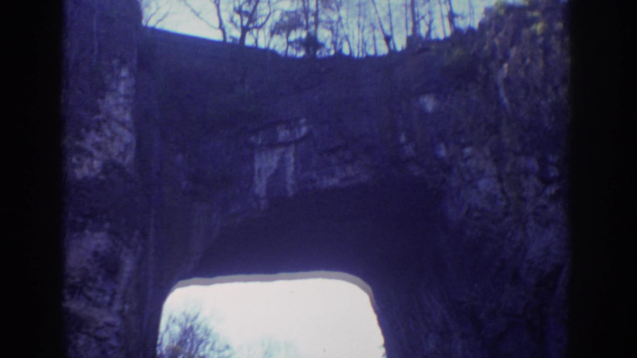 1971 Richmond, Virginia 8mm frame showing a shadowed rock arch, pale sky, and leafless trees above the cliff.