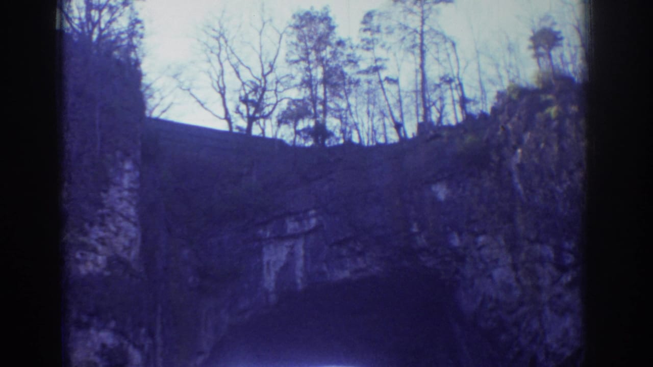 Handheld 8mm view of the Richmond rock formation, with dark stone, pale sky, and winter trees along the top edge.