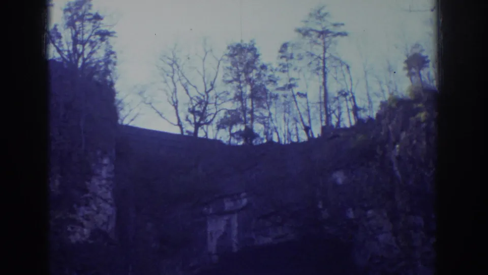 1971 Richmond 8mm frame with winter trees silhouetted above a rugged rock wall and shadowed natural arch.