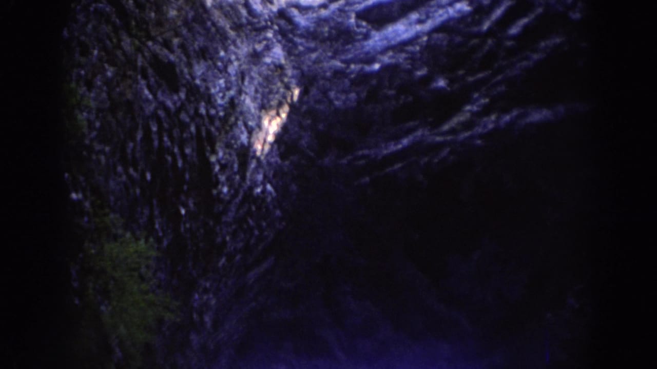 1971 Richmond-area 8mm frame looking upward from inside a shadowed rocky formation toward pale sky.