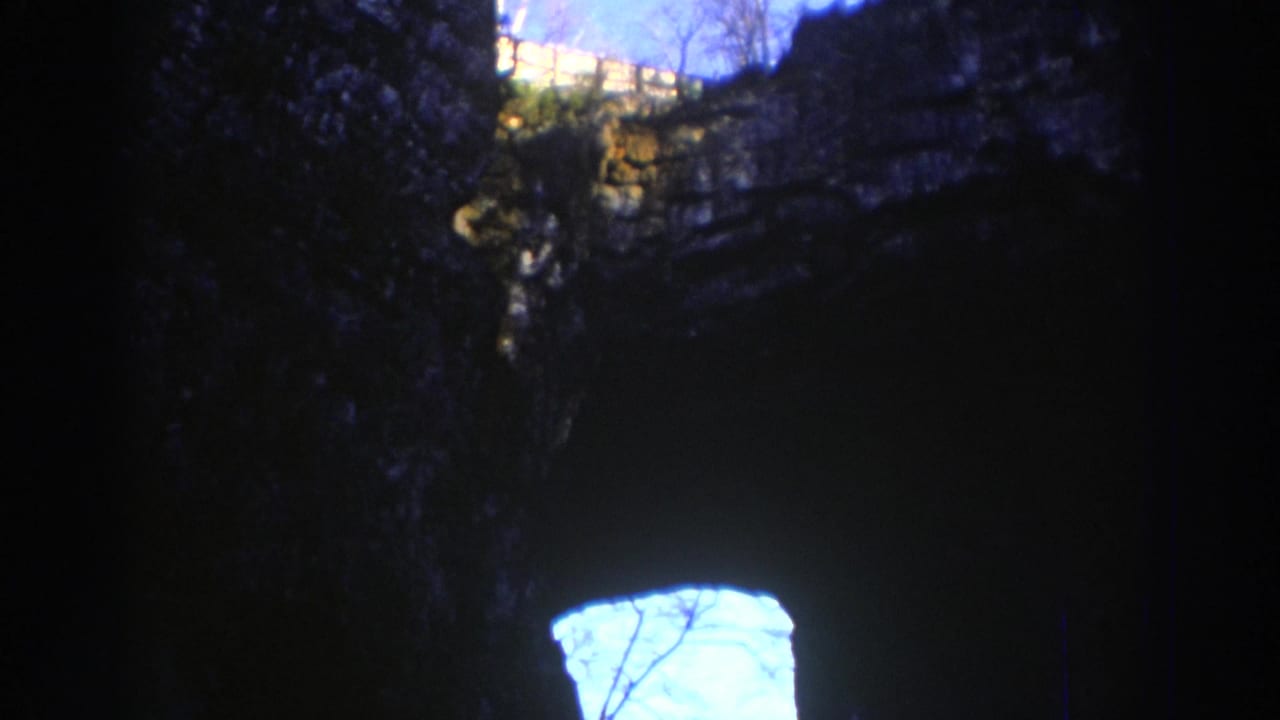 1971 Richmond, Virginia 8mm frame from inside a dark cave, looking toward a bright blue sky opening and silhouetted branches.