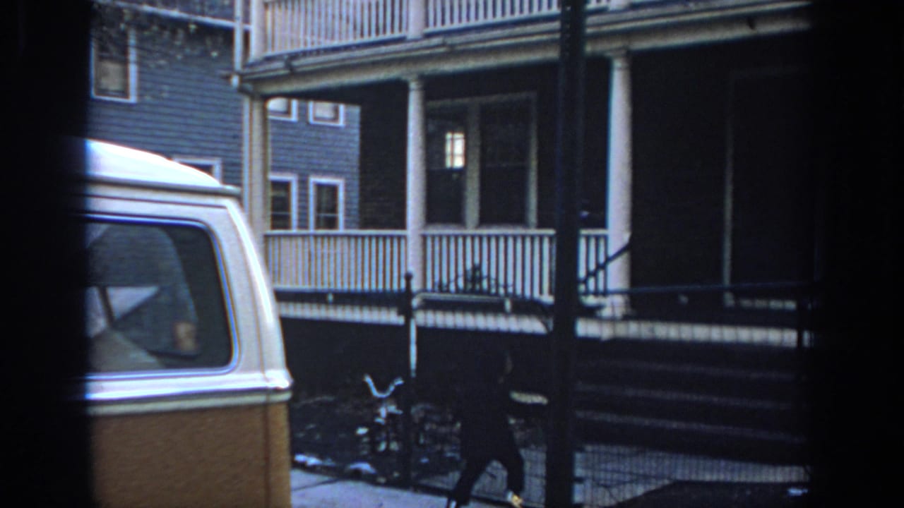 Person in dark clothing walks along the fence line near a porch and parked van.