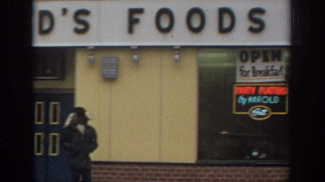 1972 Philadelphia street view of a pedestrian walking past a food storefront with breakfast and party-platter signs.