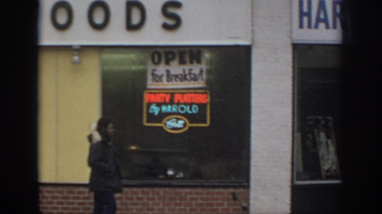 Person in a dark coat walks past a food storefront window.