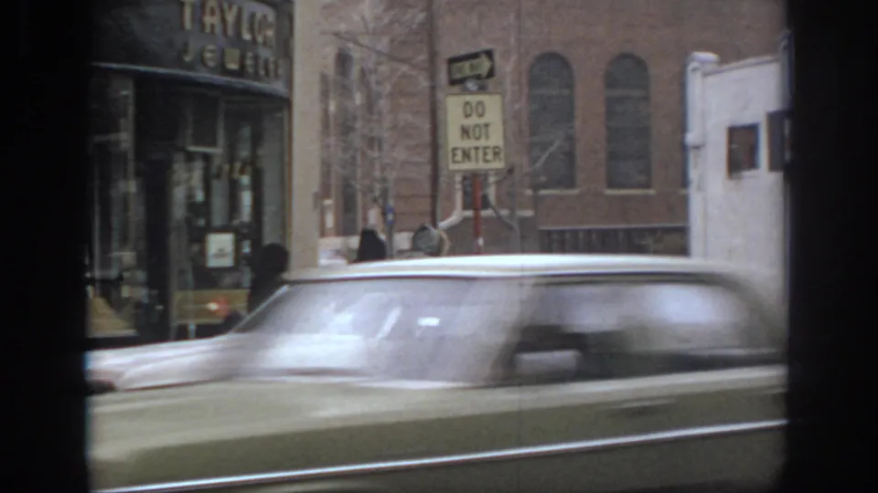 1972 Philadelphia street view with blurred traffic, storefront signage, pedestrians, and a Do Not Enter sign.