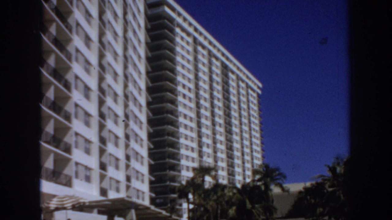 White balcony tower and adjacent high-rise building seen in bright sun.